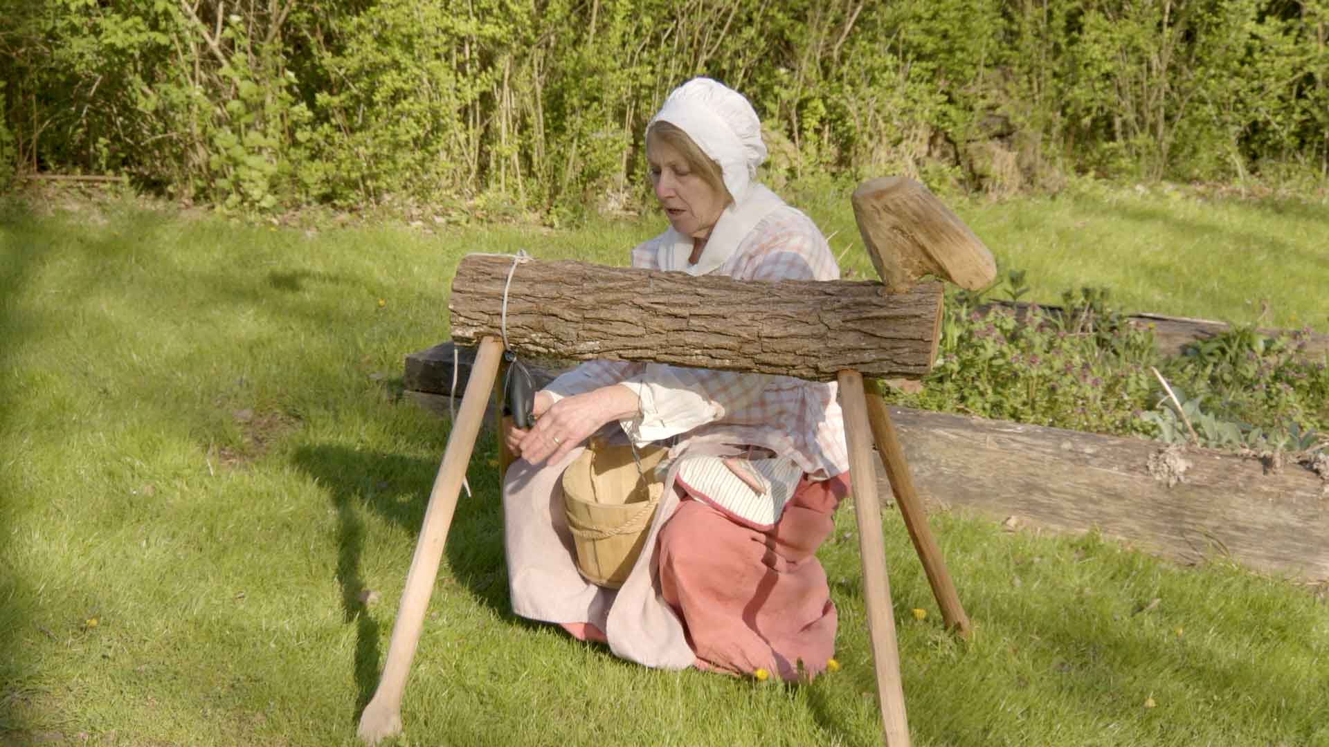women dress in colonial era clothing demonstrates how to milk a cow