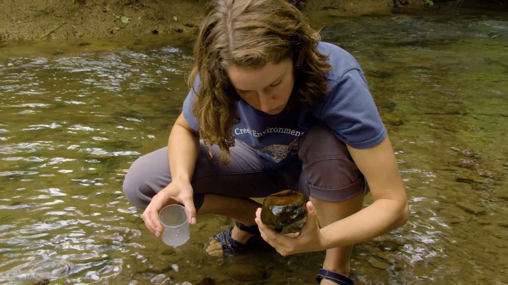 woman looking at a rock in a stream