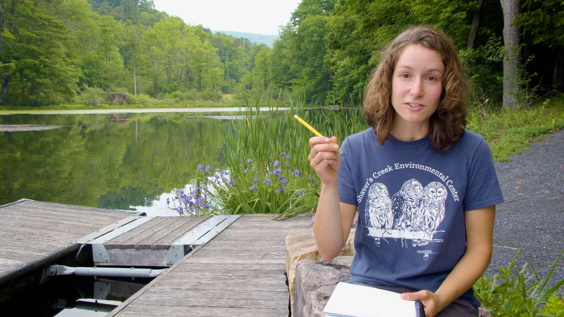woman sitting near a lake holding a pencil and notebook