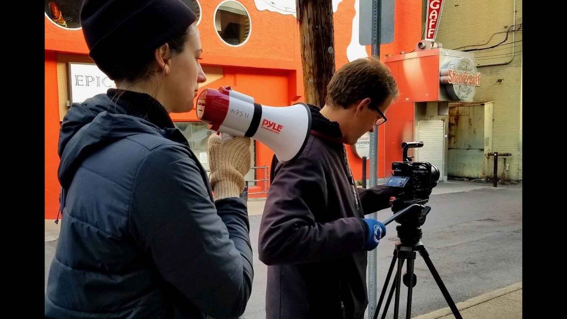 producer giving direction to technician operating a video camera on tripod